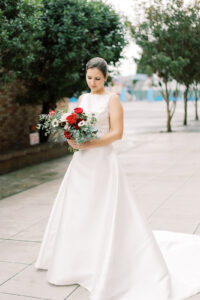 a bride in her wedding dress holding her red wedding bouquet and looking down at her bouquet outside of a church in seattle