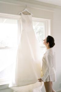 a bride looking up at her wedding dress thats hanging from a window