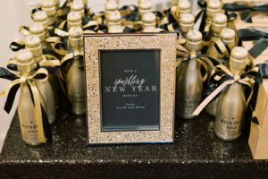 a golden picture frame with writing in it and gold champagne bottles next to it with gold and black ribbons tied on them.