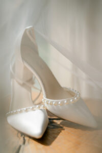 white wedding shoes shining in the sun with a wedding veil draped over them