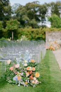 clear plastic chairs lined up for a wedding ceremony in scotland with bright colored flowers