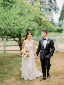 a bride and groom holding hands in an orchard and walking towards the camera