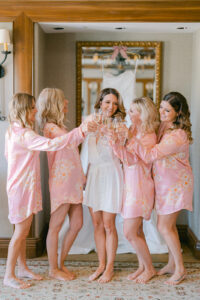 a bride and her four bridesmaids toasting with champagne in pink robes before the wedding day begins