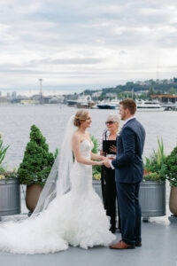 a bride and groom holding hands during their wedding at the mv skansonia in seattle with the seattle skyline behind them