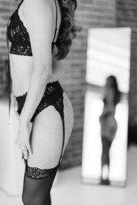 a black and white photo of a woman wearing black lingerie and looking at herself in the mirror but the mirror is blurred out and her body is in focus
