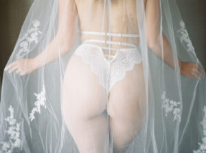 a woman's backside with white lingerie and a lace veil around her