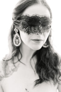 a black and white photos of a woman with a black lace blindfold and large dangly earrings 