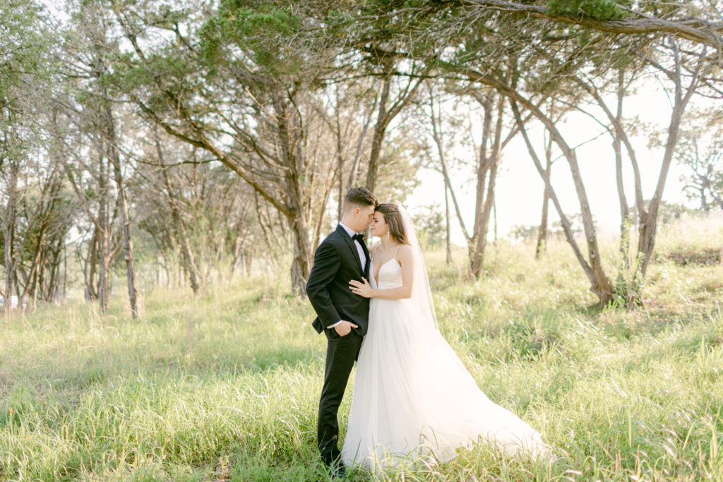 bride and groom in front of a grove of trees withe their foreheads touching