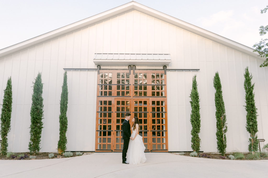 bride and groom stand in front of big sliding wooden doors at The Ivory Oak wedding venue in Texas