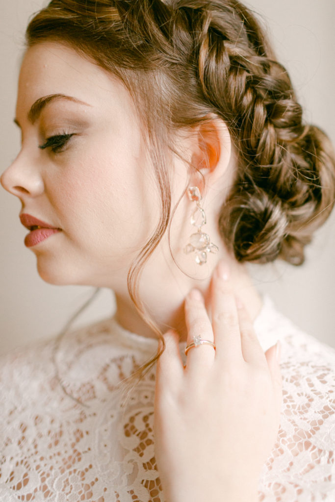 close up of a bride looking away and touching her neck while showing off her braided hair and earrings