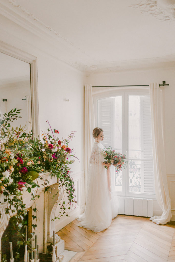 bride standing in front of paris apartment window looking down at her flowers