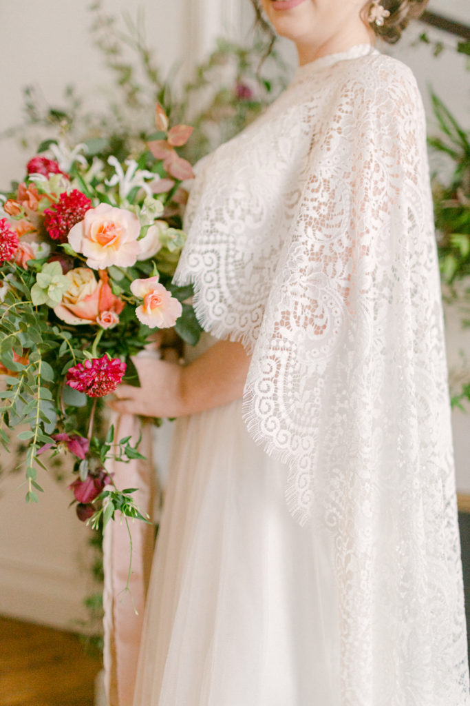 close up of bride holding her bouquet with a lace cape draped around her shoulders