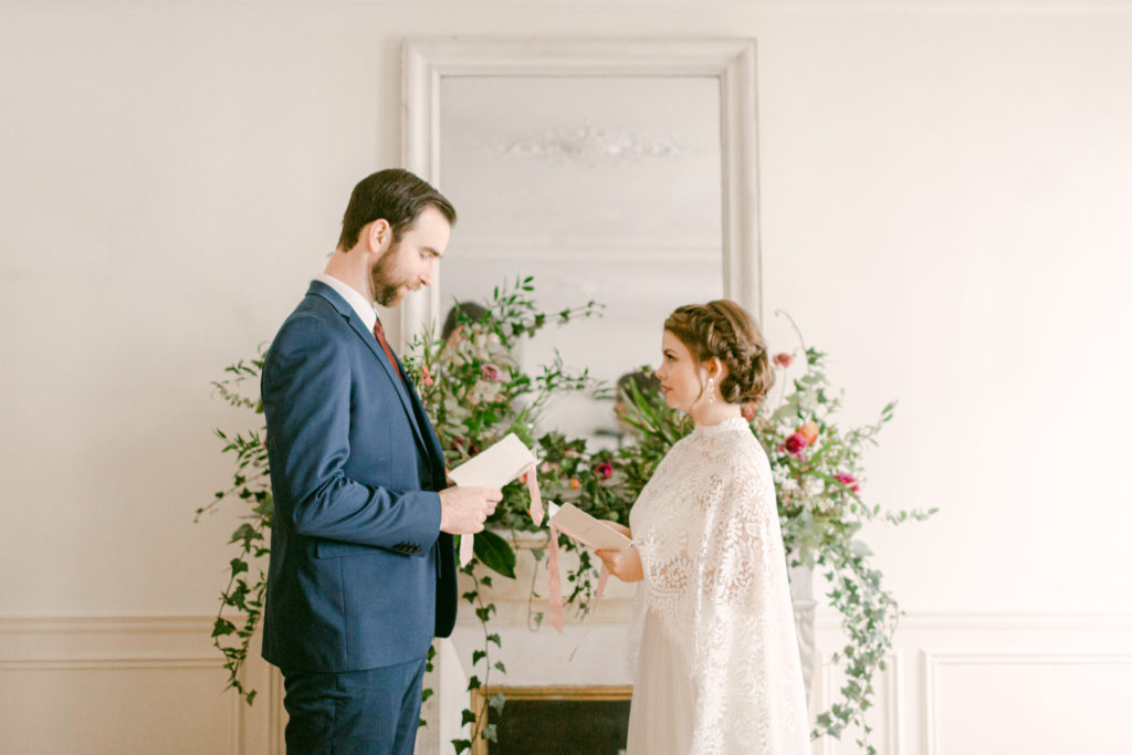Bride and groom reading their vows in front of a fireplace mantel with a floral arrangement in a paris apartment 