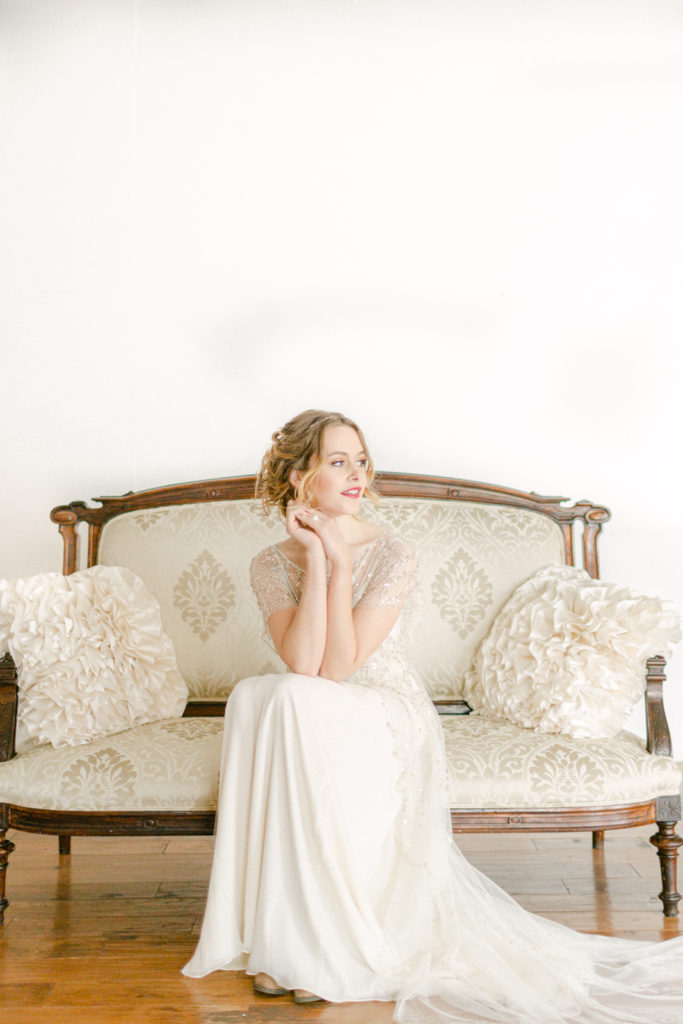 bride sitting on an old couch with her hands softly under her chin and looking away
