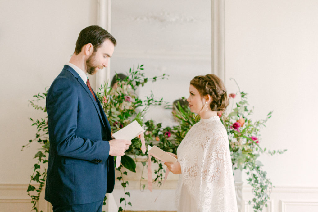 bride and groom reading vows in front of floral fireplace in Paris