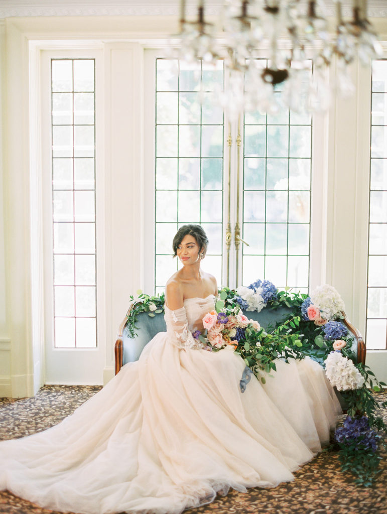 bride in a pink wedding dress sitting on a blue couch in front of a window