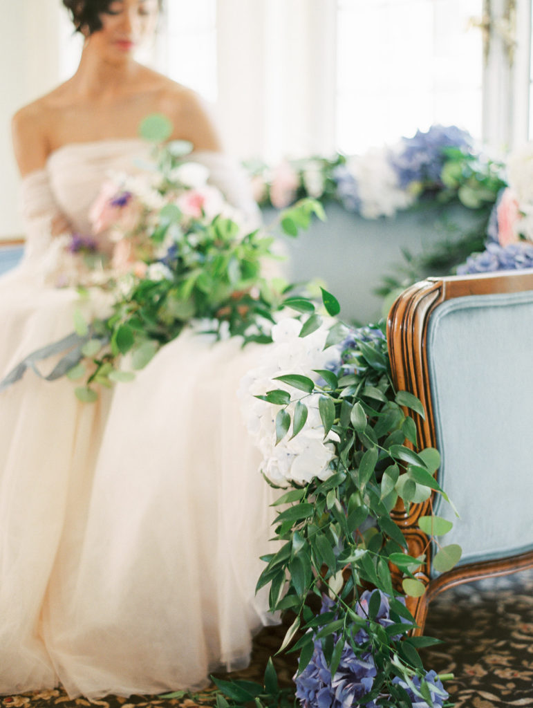 bride in a pink wedding dress holding her bouquet of flowers on a blue couch