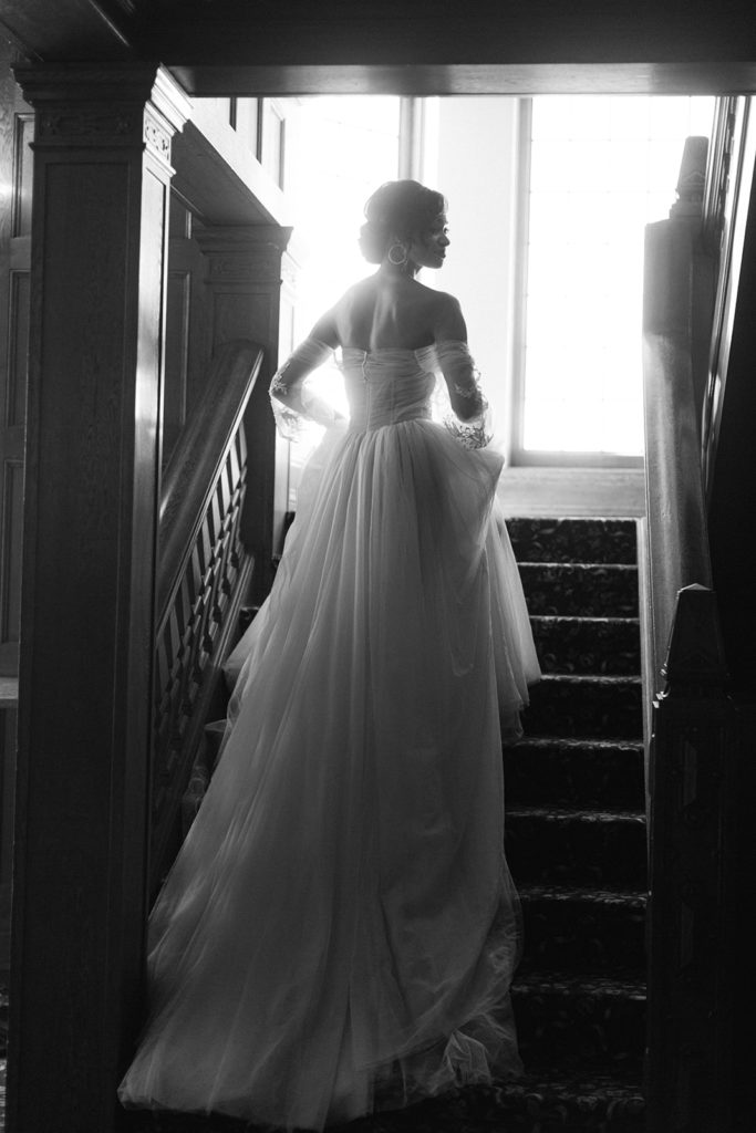 black and white image of bride walking up stairs holding her wedding gown