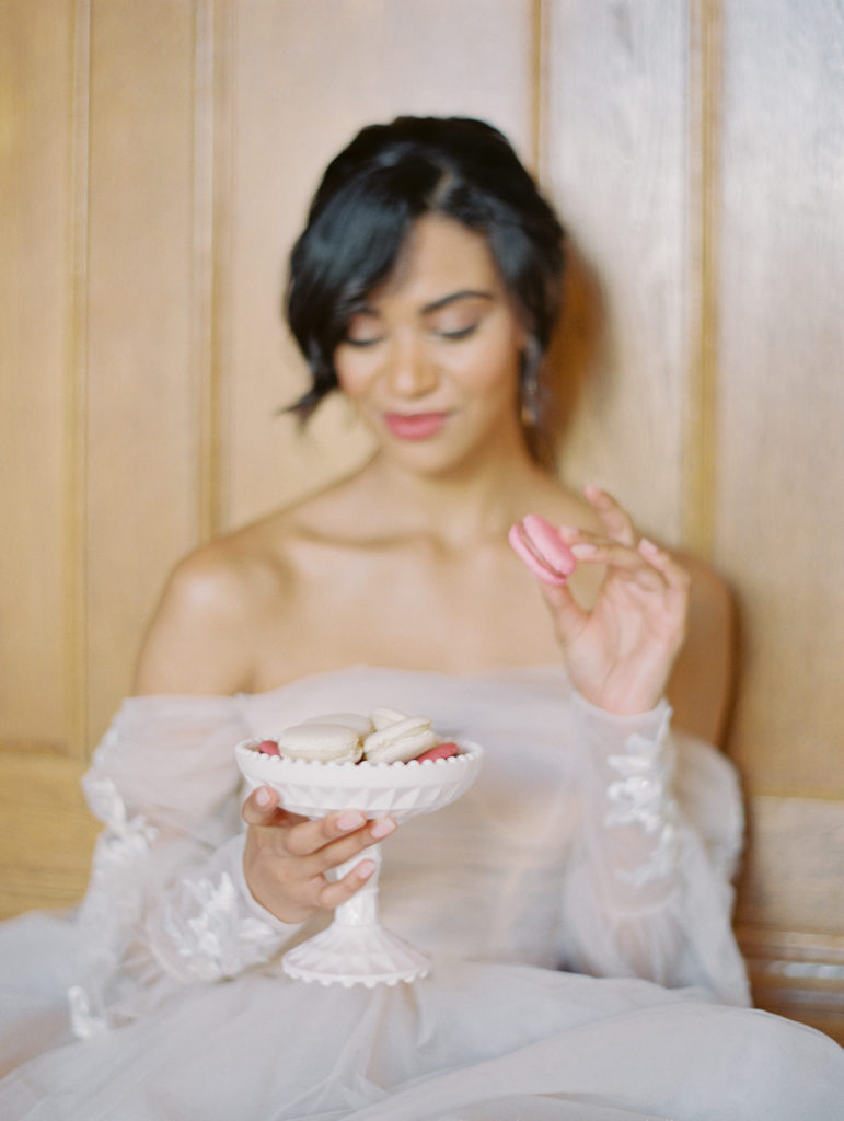 bride in pink wedding dress sitting down on the floor holding a plate of macaroons