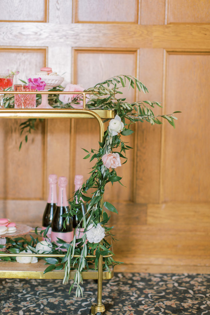 bar cart with champagne cocktails and champagne bottles with florals draping over the side
