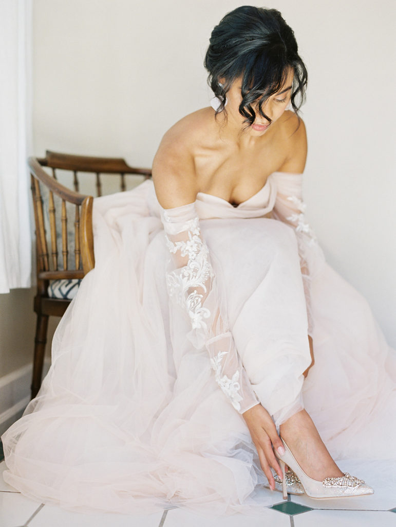 black bride in a chair wearing a pink dress putting her shoes on