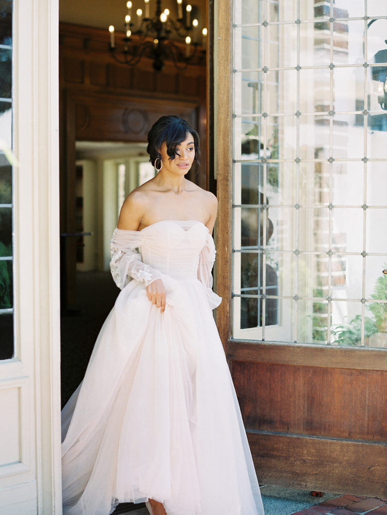 bride standing in doorway holding pink wedding dress