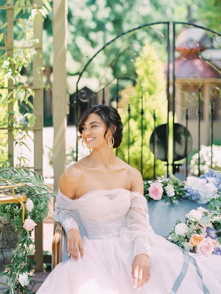 bride sitting on blue couch and wearing a pink wedding dress while laughing and looking off into the distance
