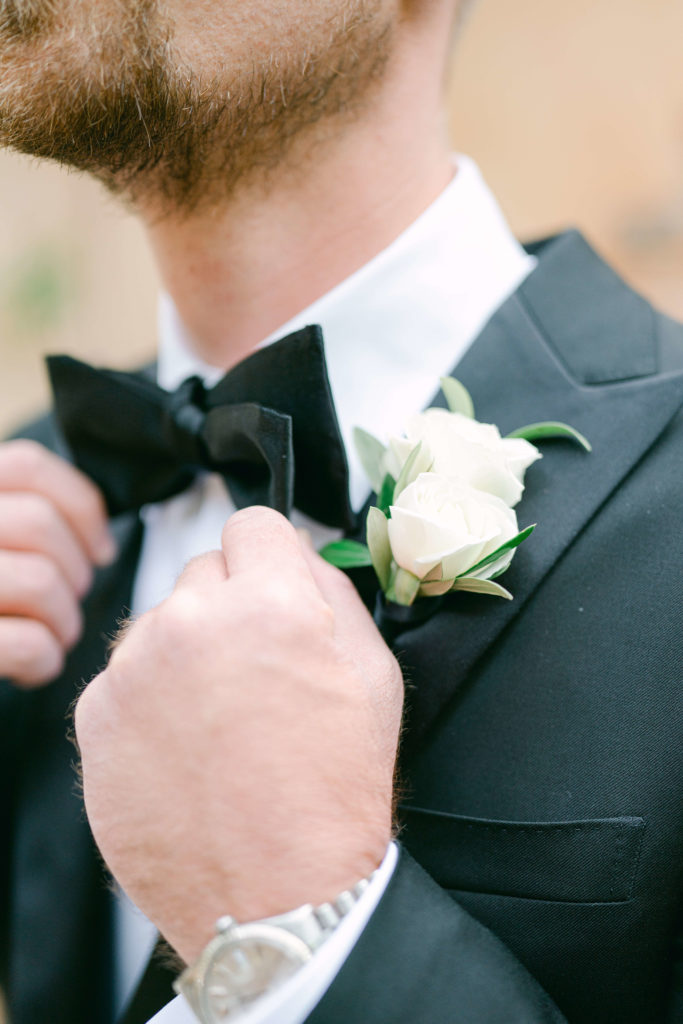 groom adjusting his bowtie next to his boutonnière  