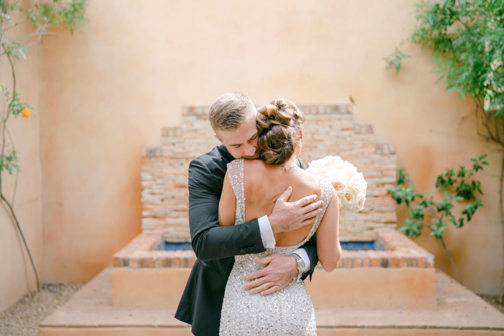 groom embraces bride in front of fountain at royal palms resort in phoenix