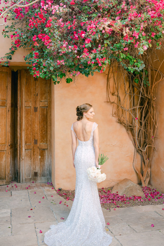 bride with her back to the camera standing under flowers with her bouquet to her side