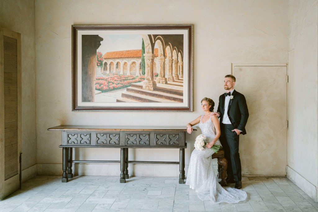 bride sitting down on a chair with grooms standing behind her in front of a portrait of the royal palms resort