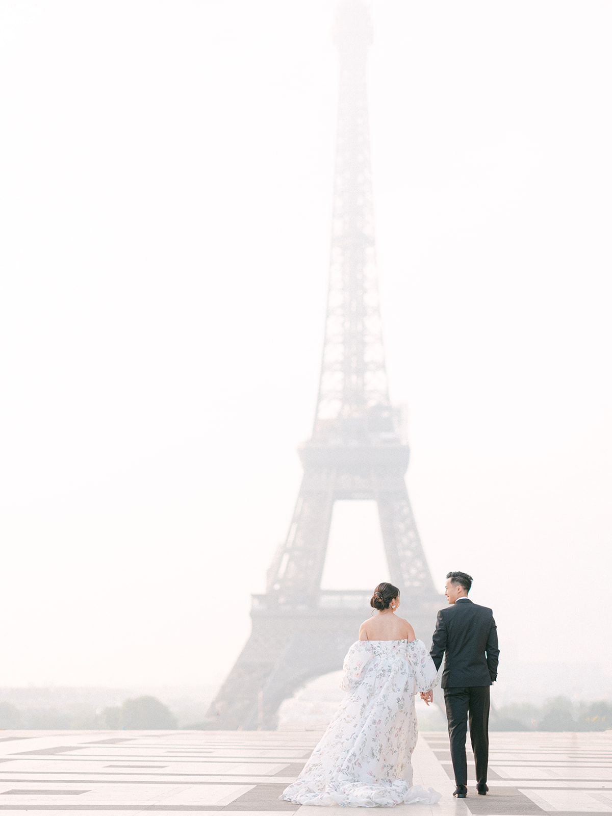 a bride and groom holding hands and walking away from the camera with the eiffel tower in the background