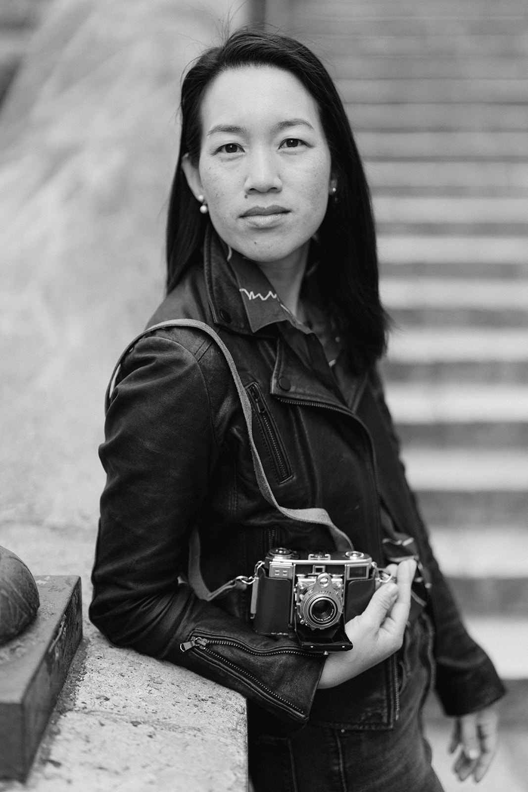 black and white photo of a woman with a camera in her hand leaning against a wall