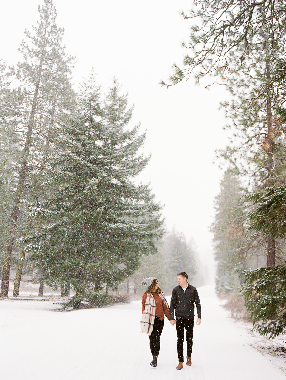 a girl and boy holding hands in the snow walking towards the camera on a snowy road in suncadia washington