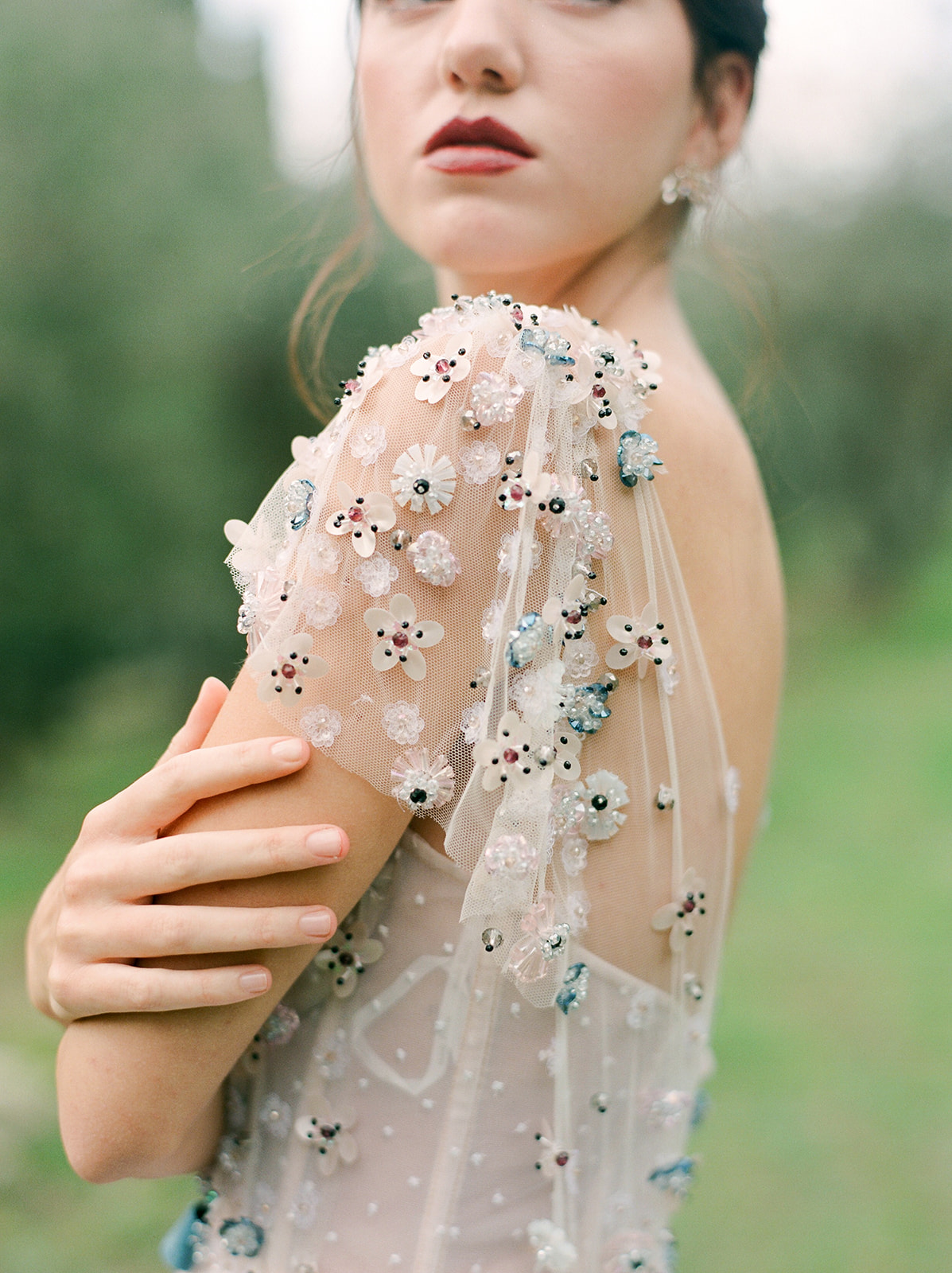 a bride in a beaded floral dress touching her arm and looking away from the camera