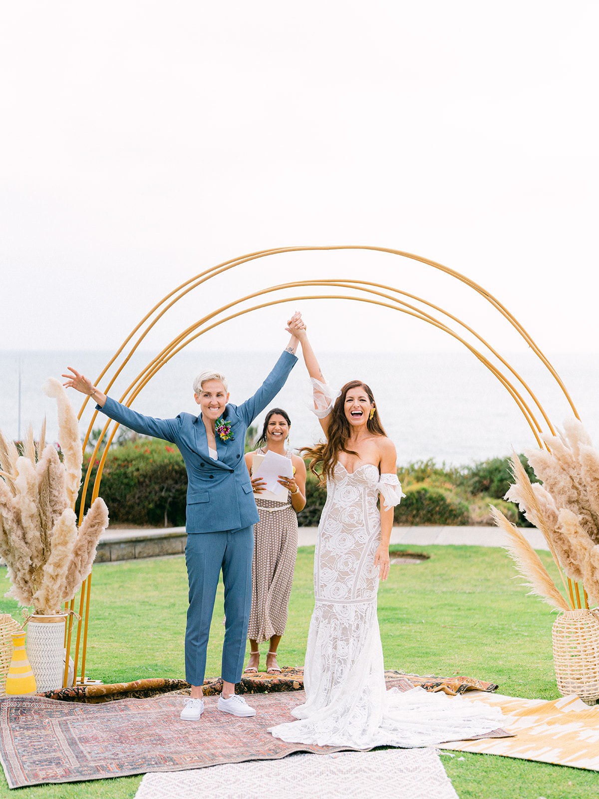 two brides celebrating with their hands in the air at their Crescent Bay beach wedding