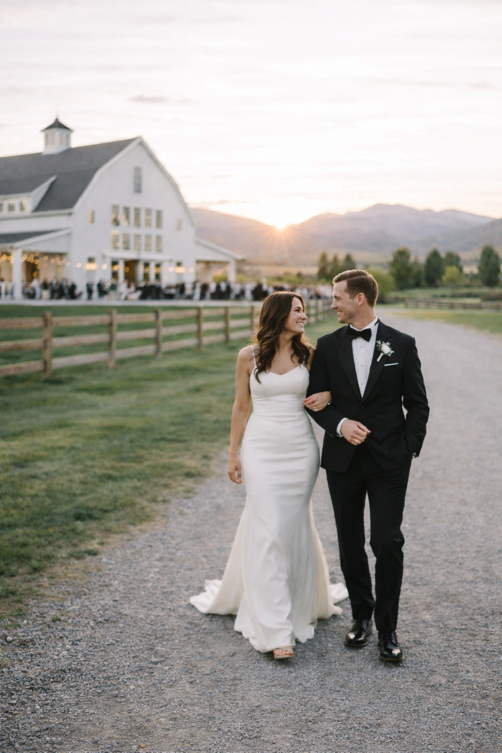 a bride and groom holding hands and walking away while smiling at each other at their river bottoms ranch wedding during sunset
