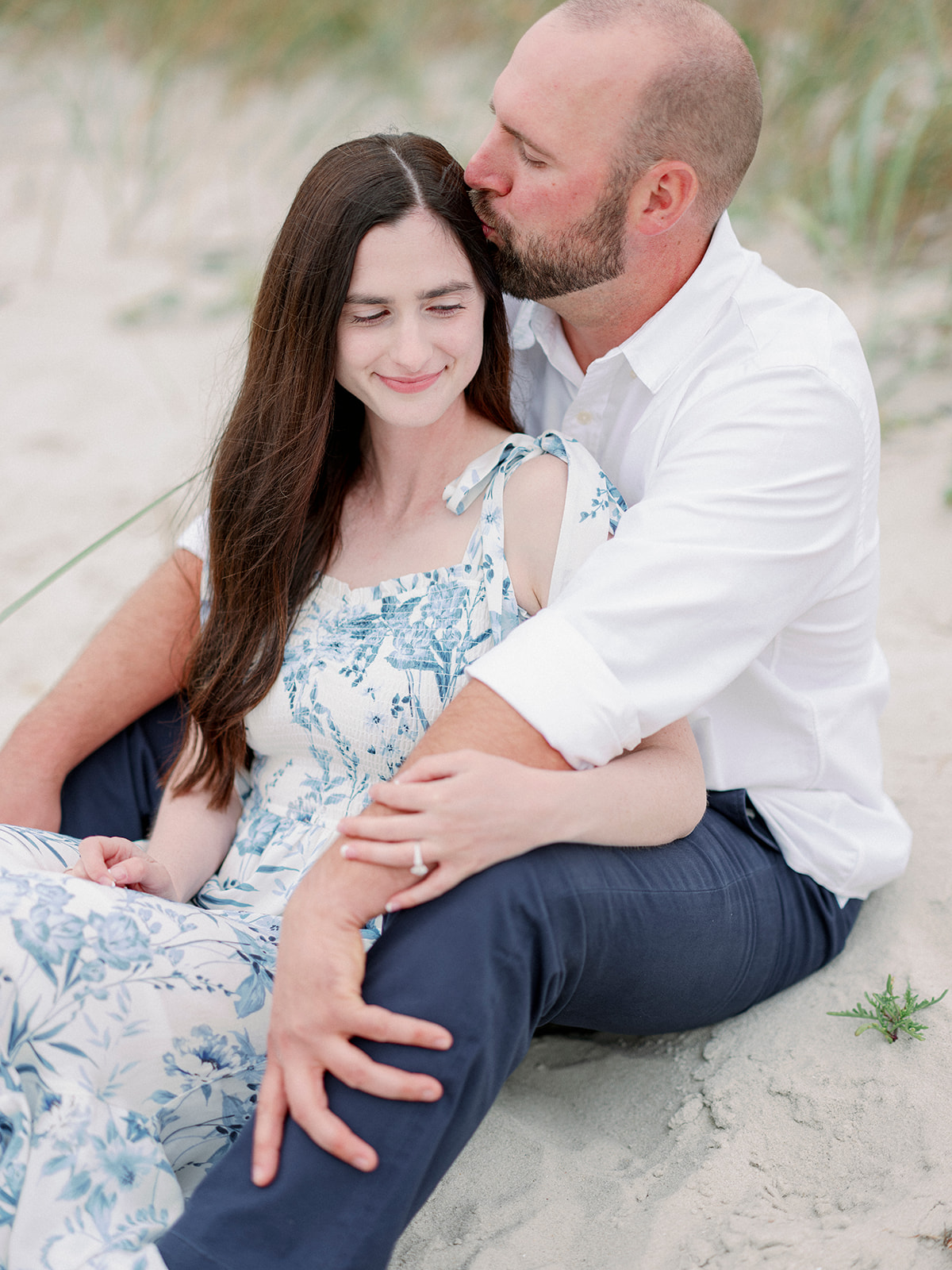 a man and woman sitting down and cuddling on the sand at their california beach engagement session in monterey beach