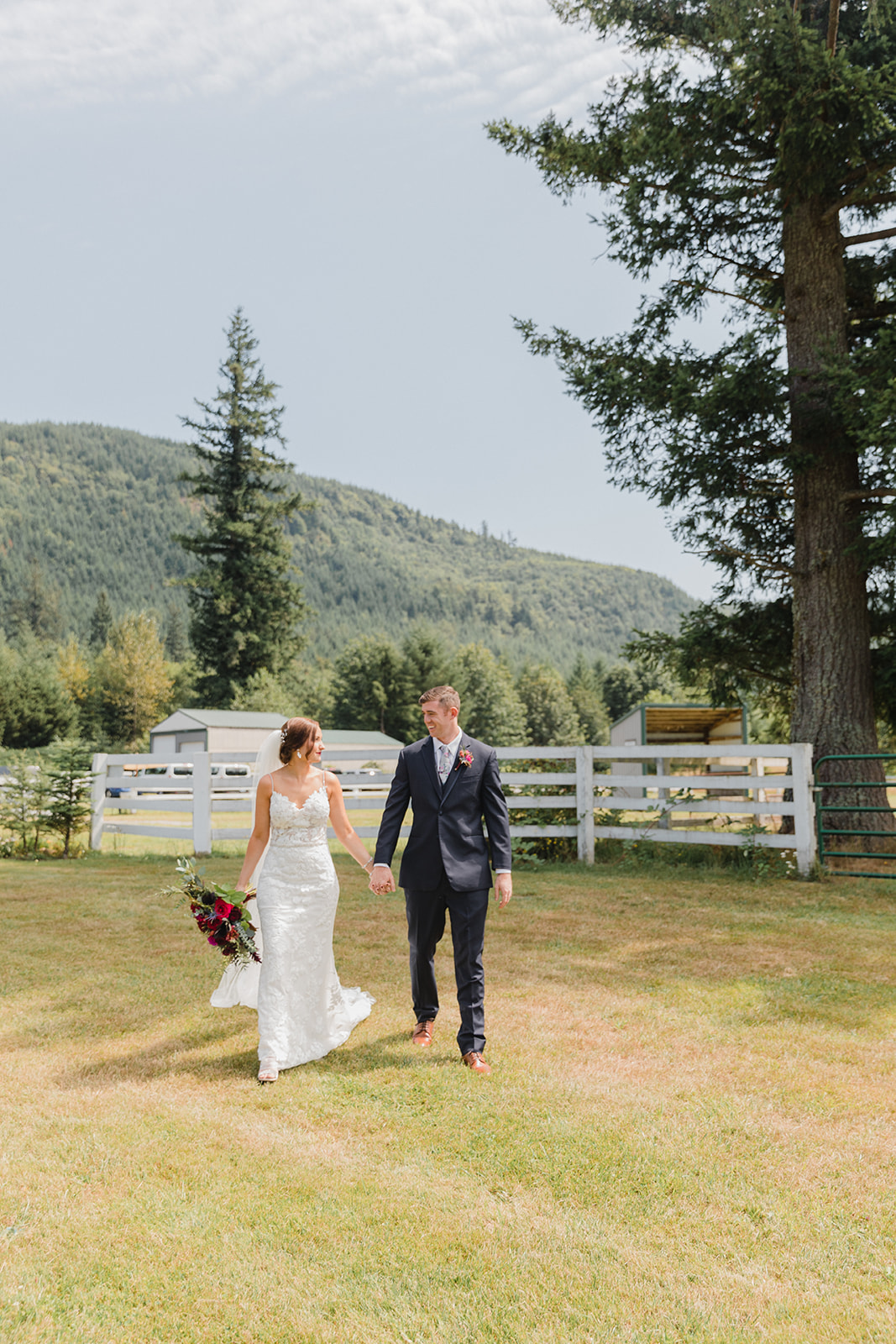 a bride and groom walking towards the camera looking at each other and smiling with a mountain behind them at their fox hollow farm wedding venue