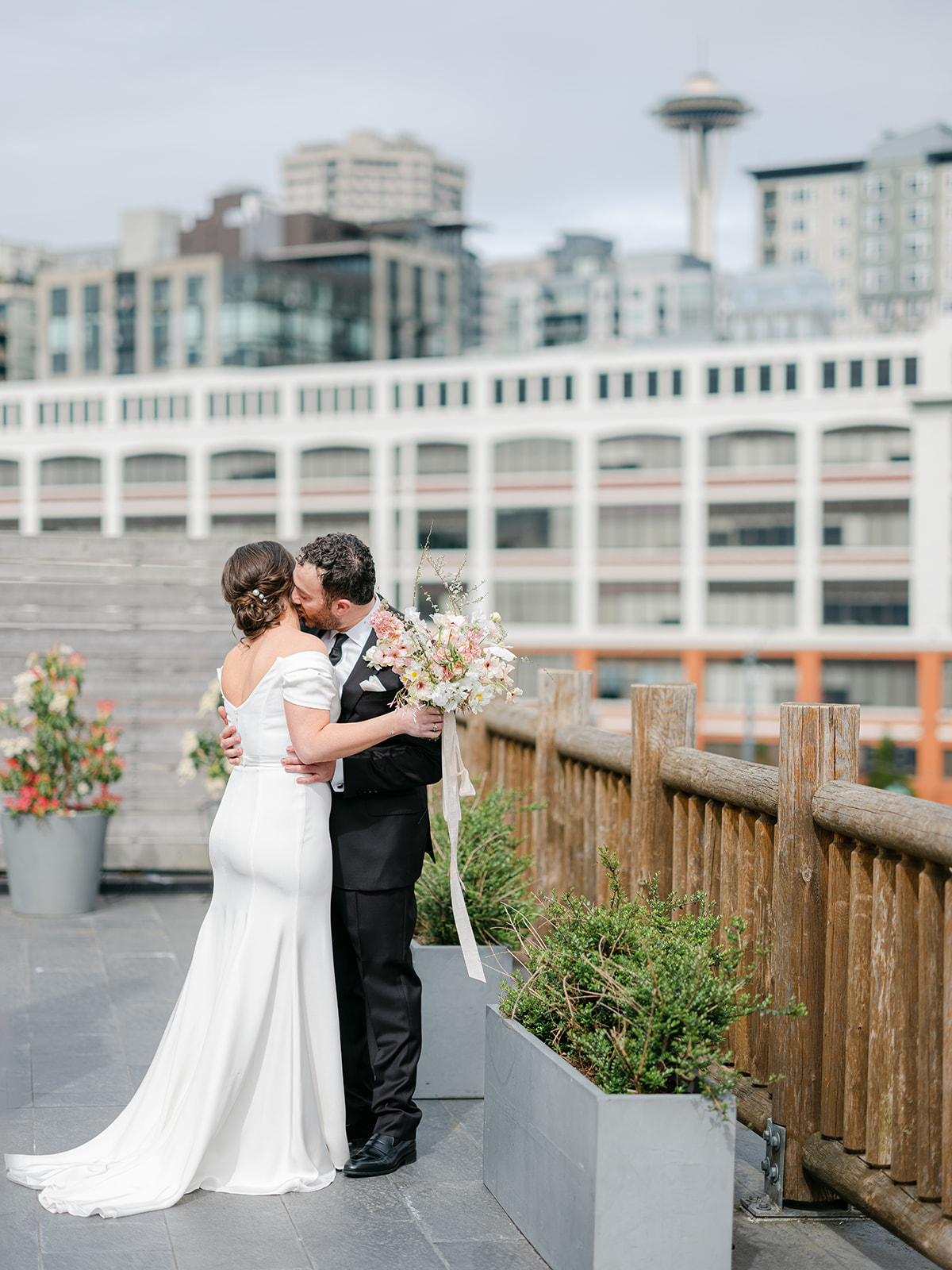 a groom kissing his bride on the neck with the seattle skyline behind them at their edgewater hotel weddings