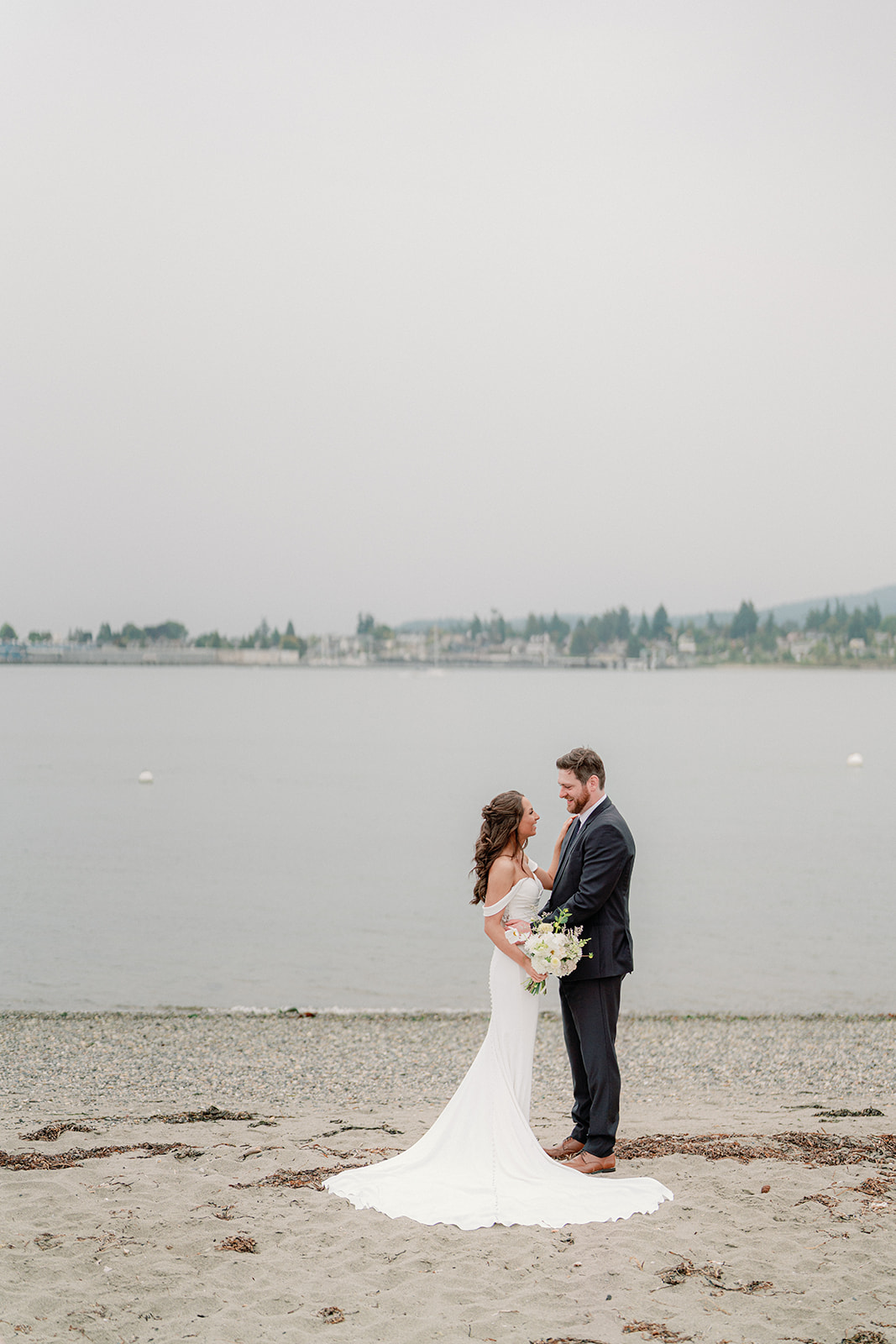 a bride and groom standing on a beach at their backyard wedding on guemes island