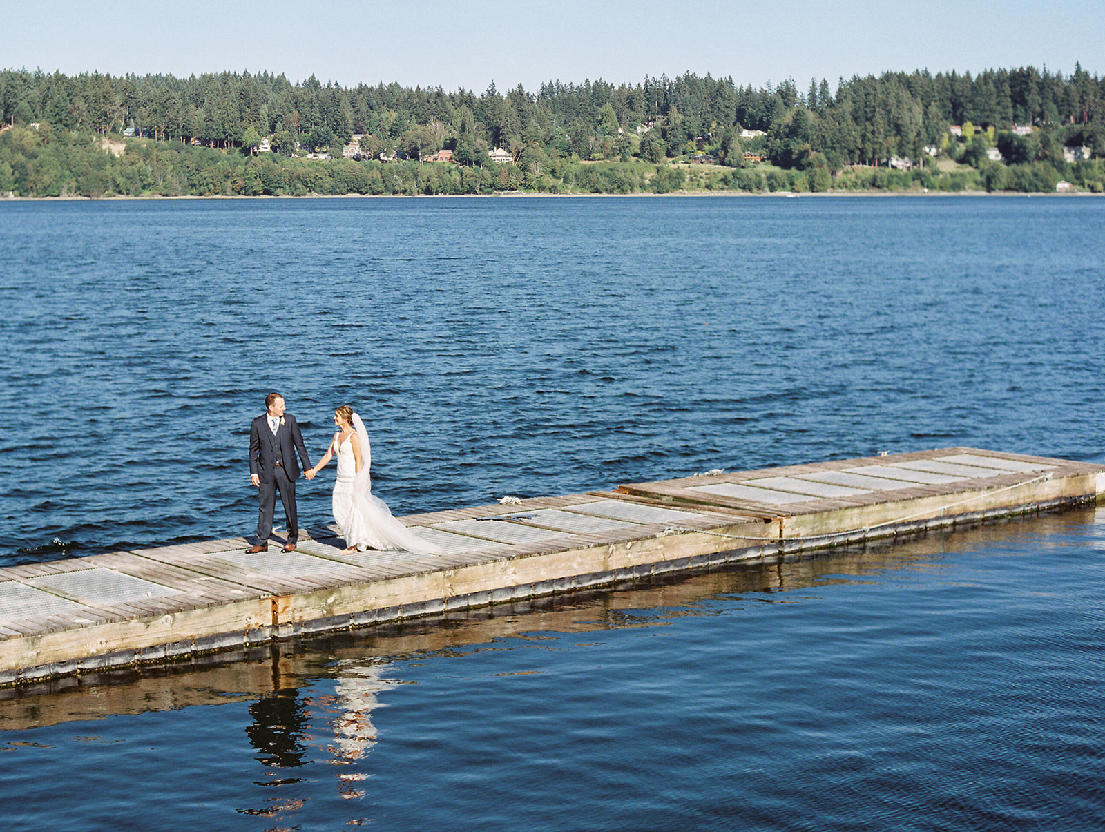 a bride and groom walking on a dock at their kiana lodge wedding