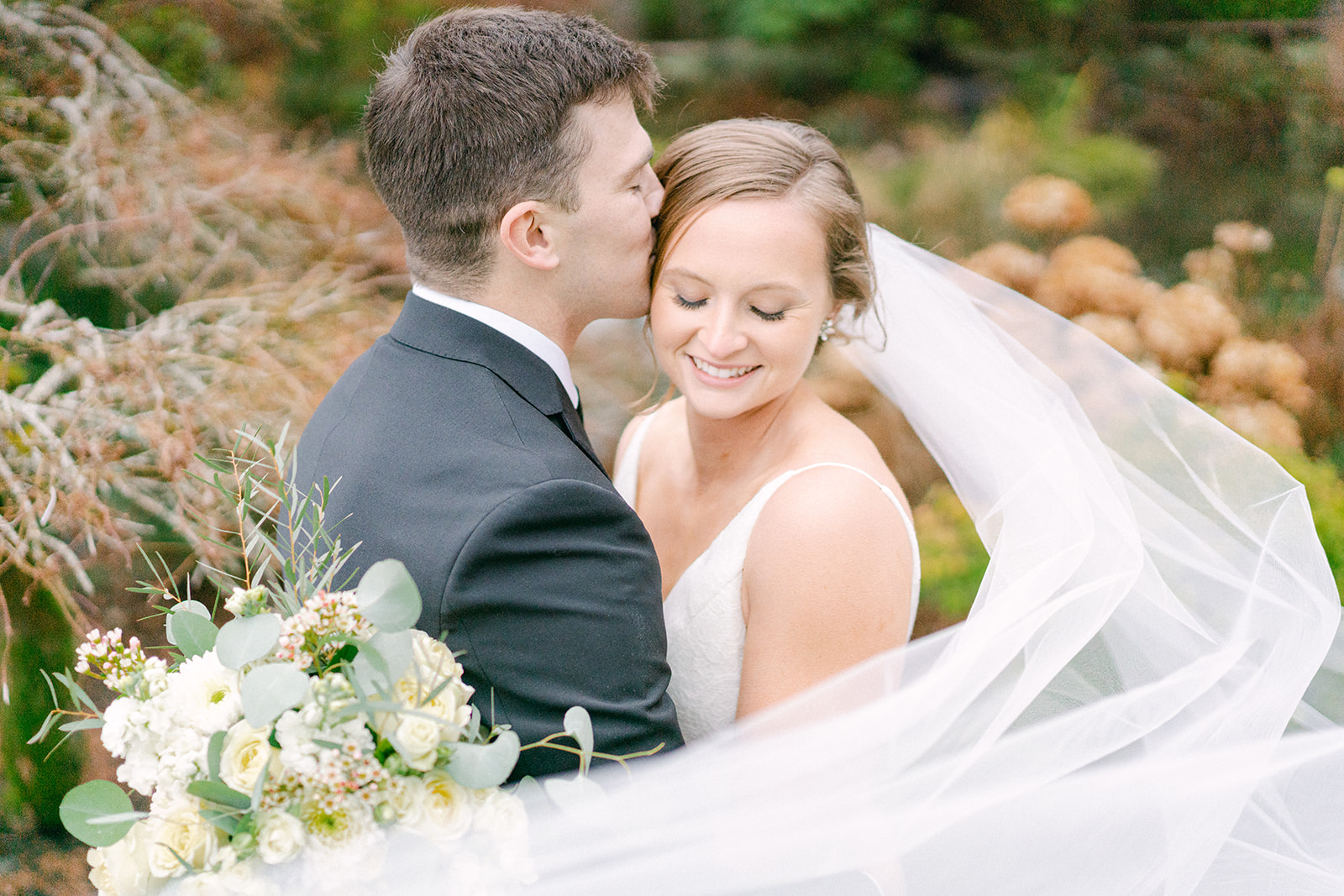 a bride with her eyes down and her groom is kissing her forehead
