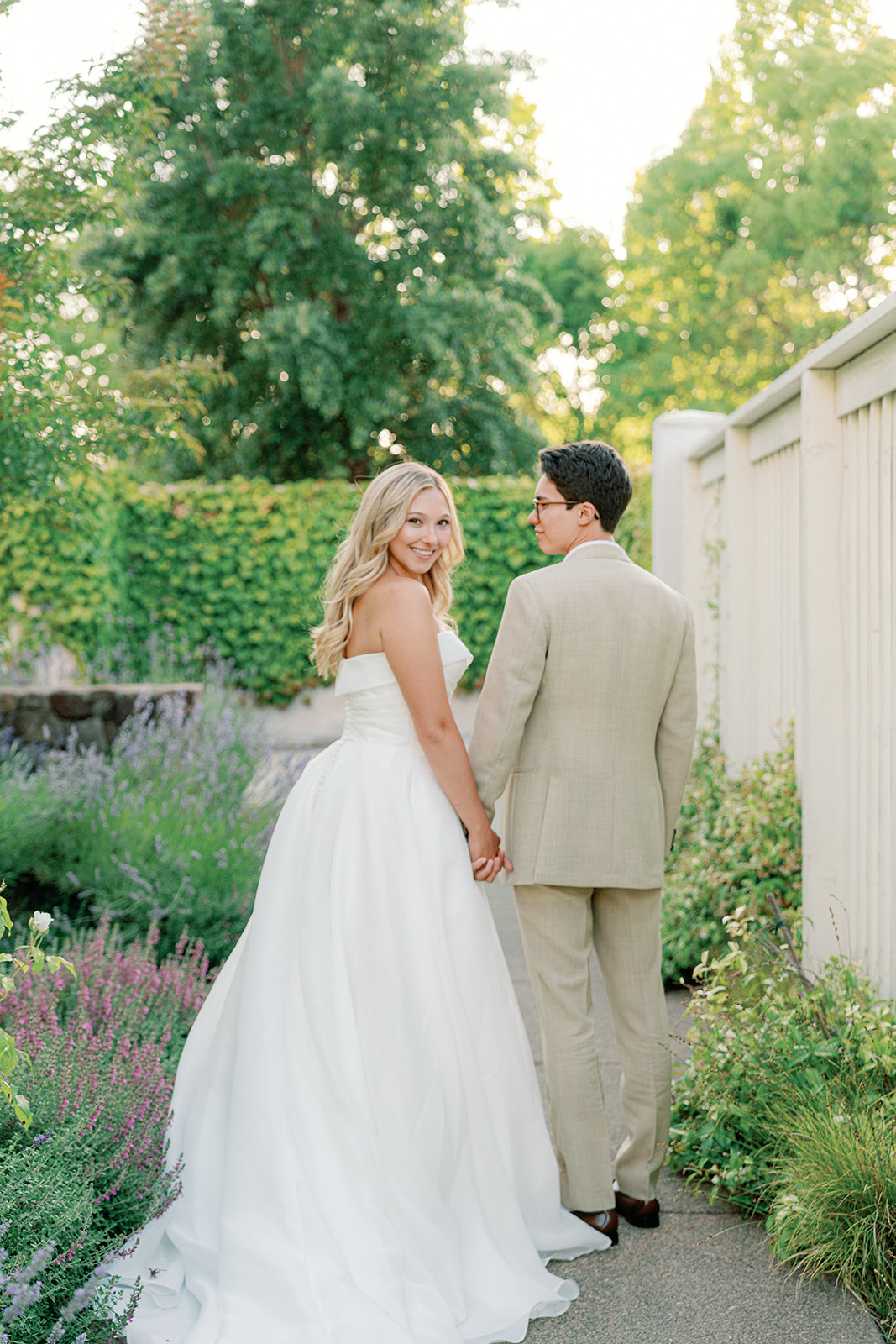 a bride and groom holding hands and walking away as the bride looks back at the camera at their sonoma wedding venue