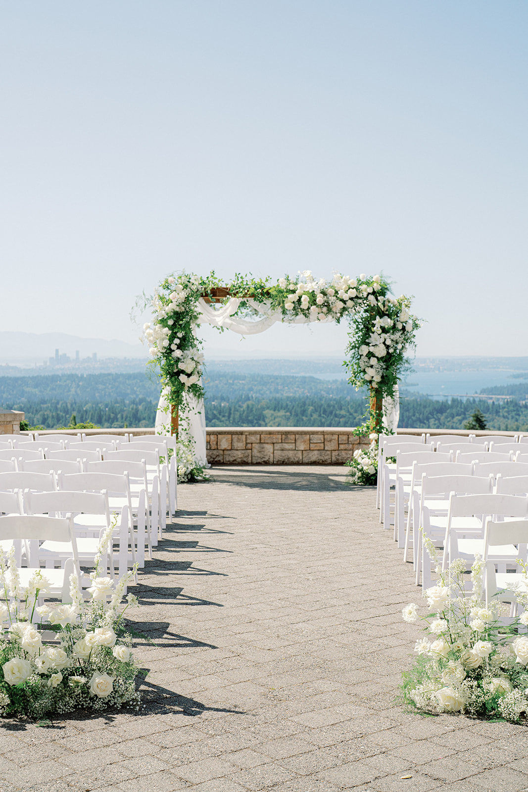 a wedding ceremony site with white chairs and white and green florals overlooking the seattle skyline at a wedding at newcastle golf club