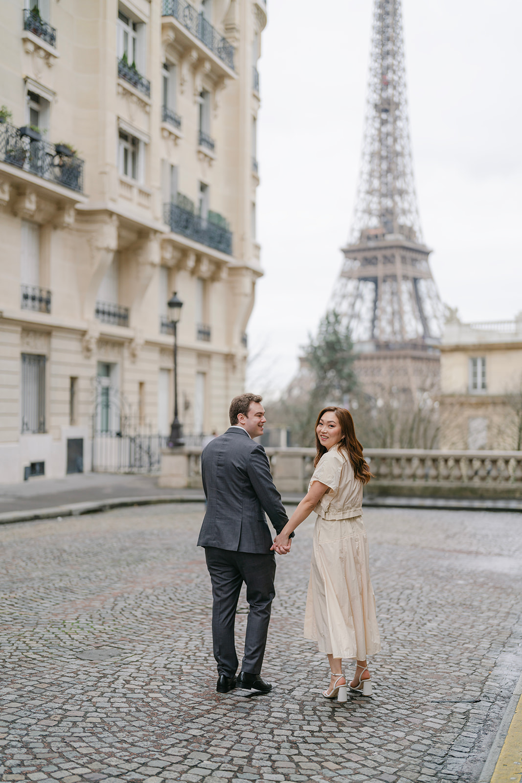 a couple walking away from the camera and towards the eiffel tower during their engagement session in paris