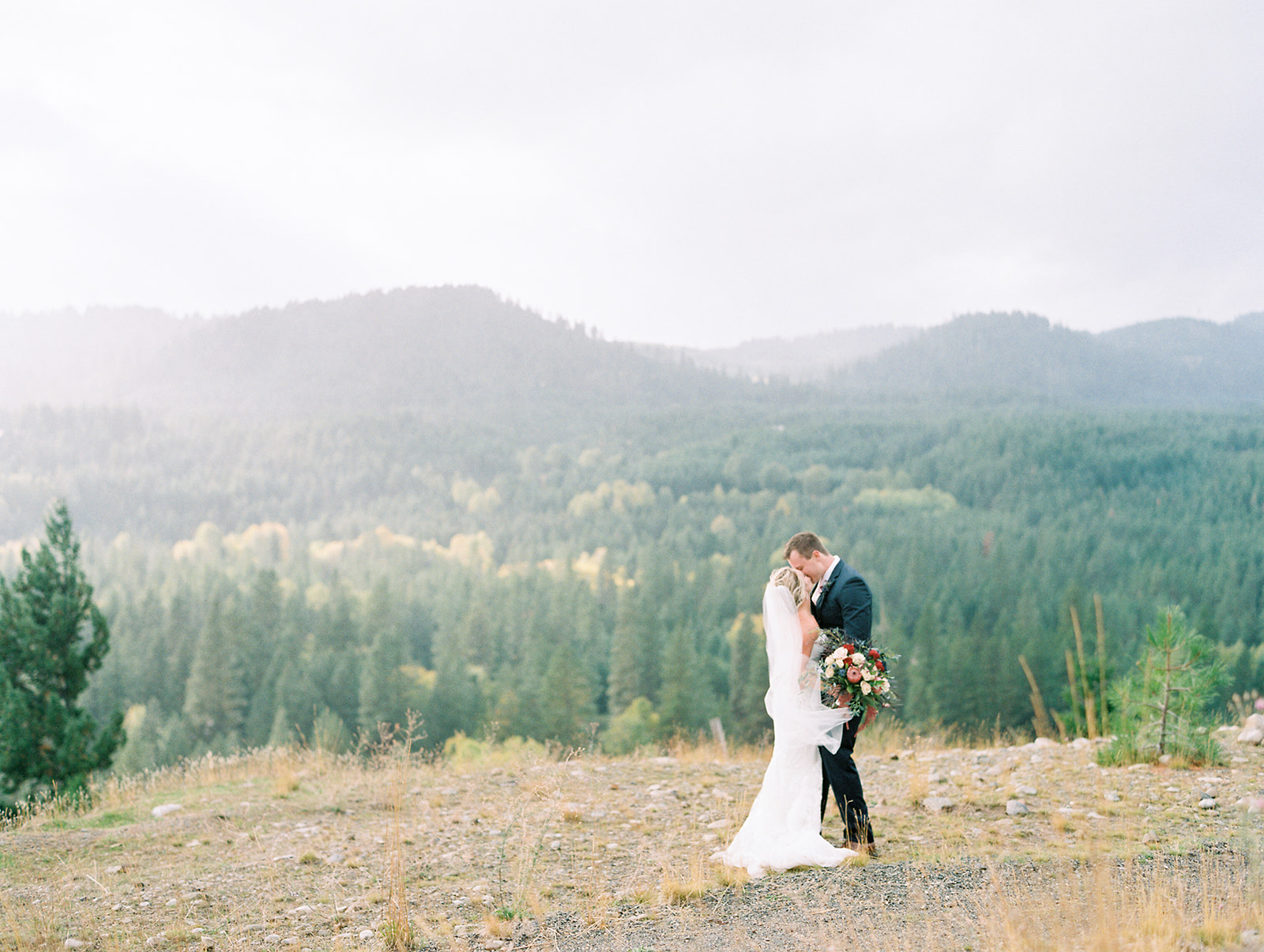 a bride and groom kissing while it rains with mountains in the background at this micro wedding venues in utah