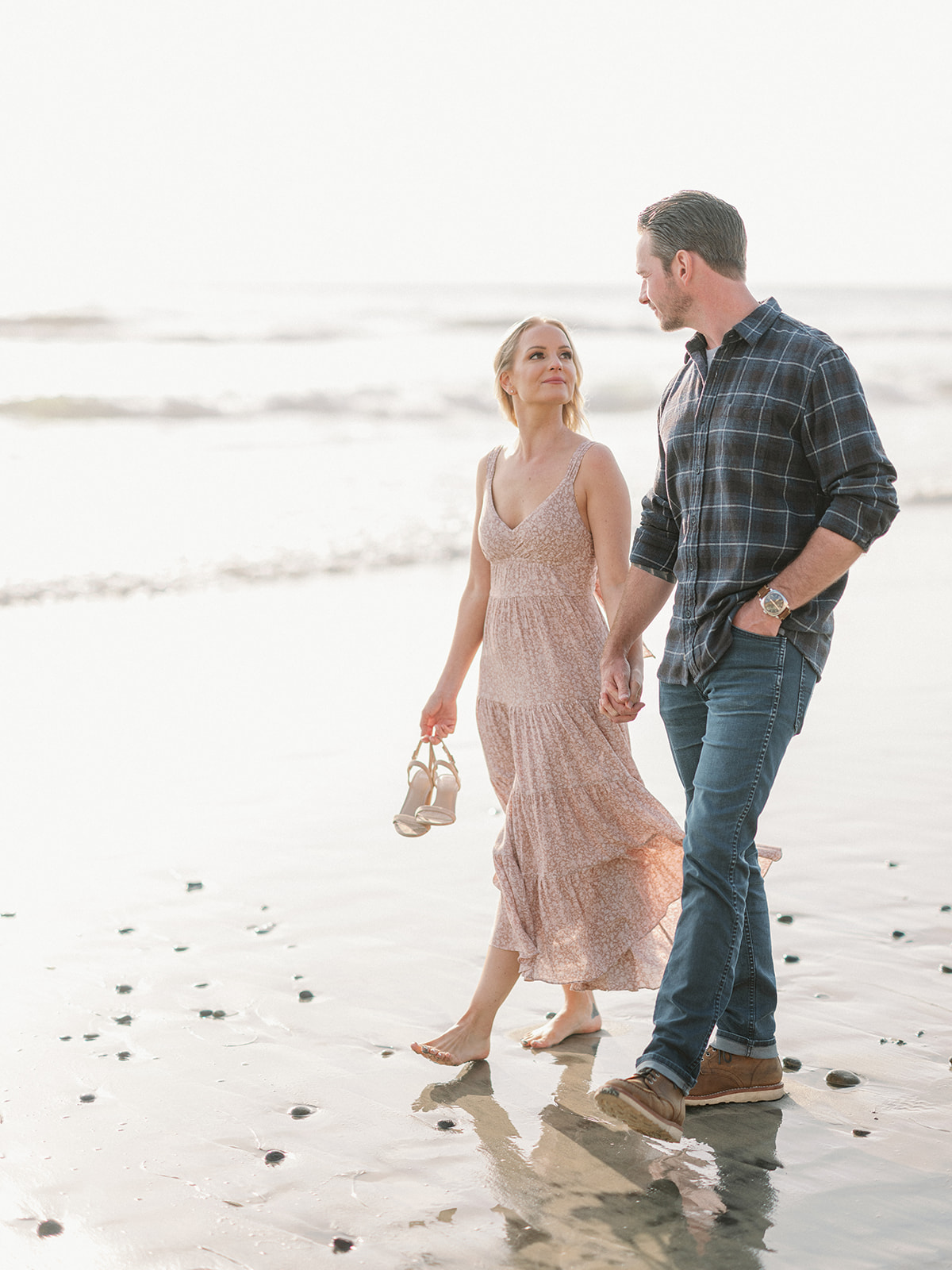 a man and woman walking hand in hand on at their engagement session at torrey pines beach.