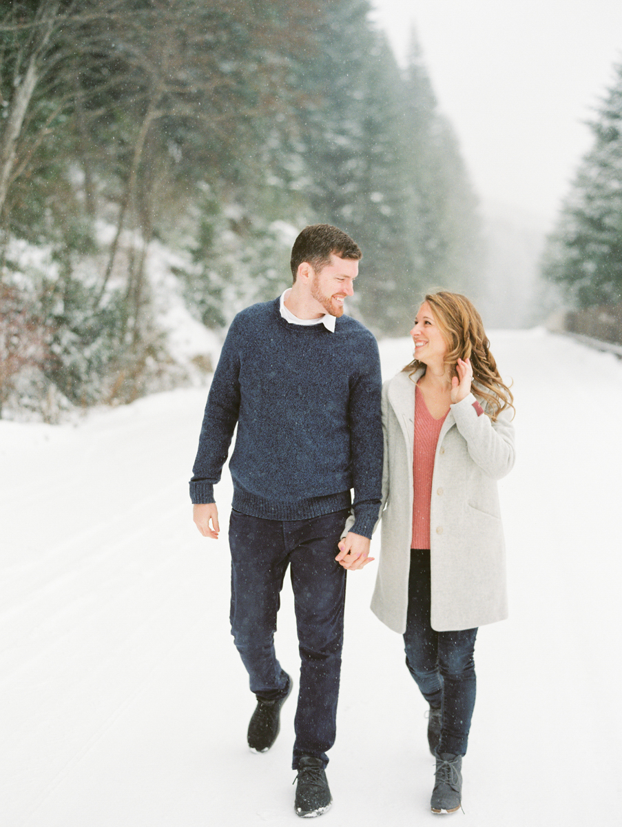 a couple holding hands and walking towards the camera for their winter engagement session