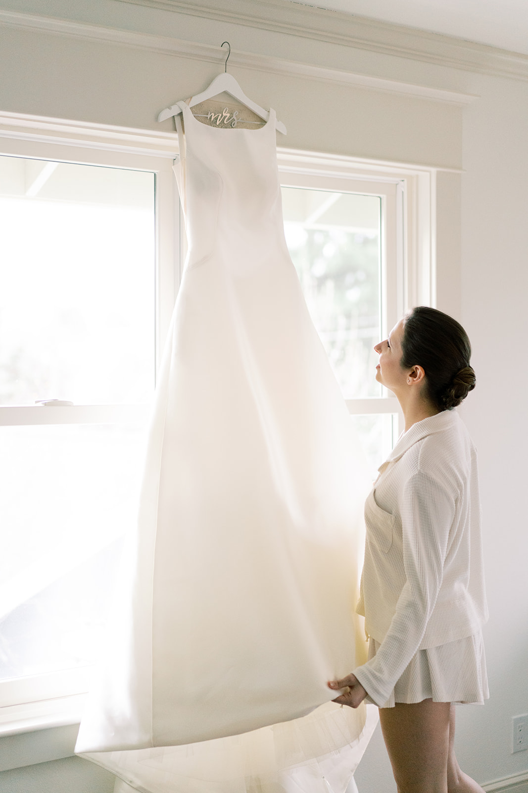 a bride looking up at her wedding dress thats hanging from a window captured by a seattle wedding photographer